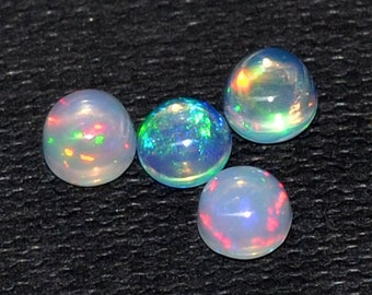 May include: A collection of nine round opals, each displaying a play of color with flashes of red, green, and blue. The opals are set against a dark, textured background, showcasing their iridescent qualities. These gemstones are ideal for jewelry making.