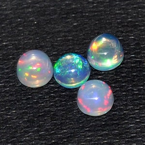 May include: A collection of nine round opals, each displaying a play of color with flashes of red, green, and blue. The opals are set against a dark, textured background, showcasing their iridescent qualities. These gemstones are ideal for jewelry making.