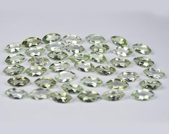 May include: A collection of numerous loose, faceted gemstones in a marquise cut. Each stone features a pale, translucent light green color with sharp, geometric facets that reflect light across their surfaces, arranged in a scattered formation.