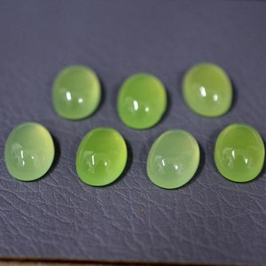 May include: Seven oval-shaped green gemstones, likely chalcedony, on a grey textured surface.