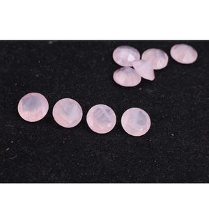 Puede incluir: Colecci&oacute;n de gemas facetadas de color rosa p&aacute;lido. Las gemas son redondas con una parte posterior plana y una parte superior multifac&eacute;tica. Las gemas est&aacute;n dispersas sobre una superficie negra, algunas agrupadas y otras espaciadas.