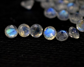 May include: A row of six iridescent moonstone gemstones, each with a round, faceted shape. The stones are arranged in a line on a black surface, with the light reflecting off their surfaces.