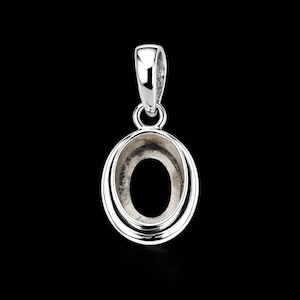 Peut inclure: Un pendentif ovale argenté avec une boucle pour une chaîne. Le pendentif a un centre creux et un cadre ovale à double couche. Le fond est noir.