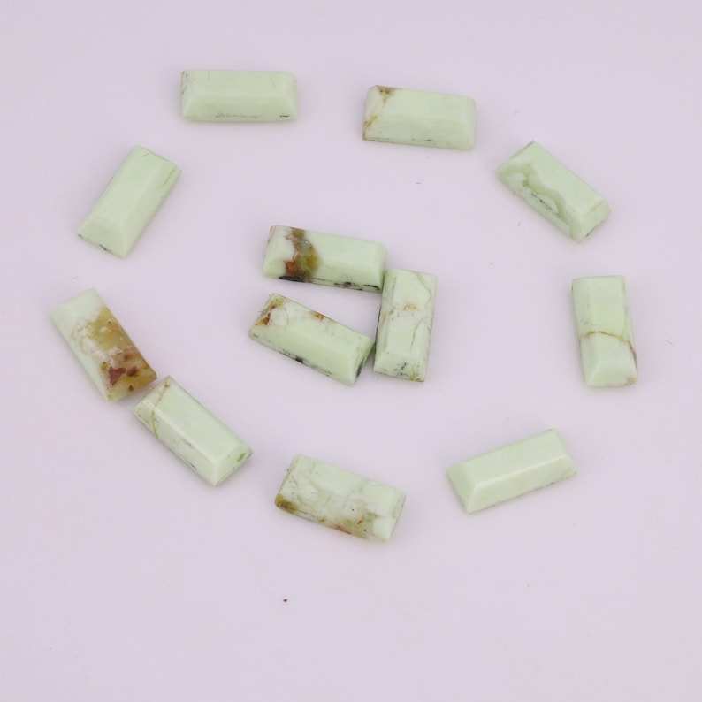 May include: A collection of eleven green and white rectangular cabochons, likely made of green opal, arranged in a circle on a white background.