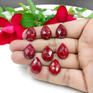 May include: Eight faceted, teardrop-shaped, red gemstones. The gemstones are arranged in two rows on a hand.