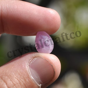 May include: A teardrop-shaped, light pink gemstone with a smooth, polished surface.