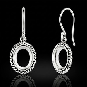 May include: Two silver oval earrings with a rope-style edge. The earrings have a hook fastening and a shiny finish, reflecting light against a black backdrop. The oval shape is open in the middle, designed to hold a stone or other embellishment.