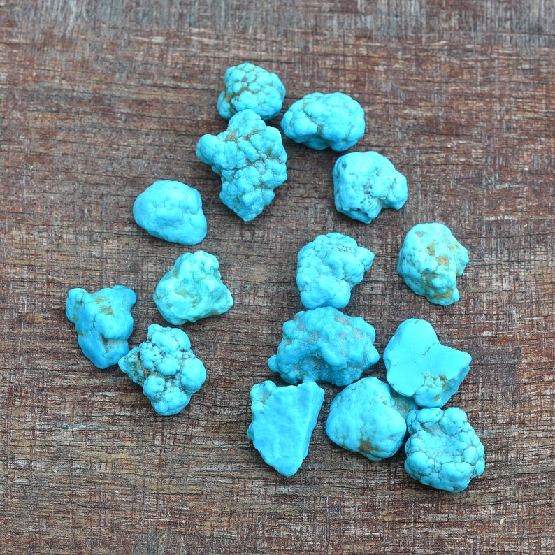 May include: A collection of turquoise stones of various sizes and shapes, displayed on a wooden surface.