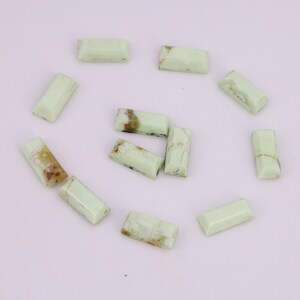 May include: A collection of twelve green, rectangular, polished, gemstone cabochons. The cabochons have a light green color with brown and black inclusions.