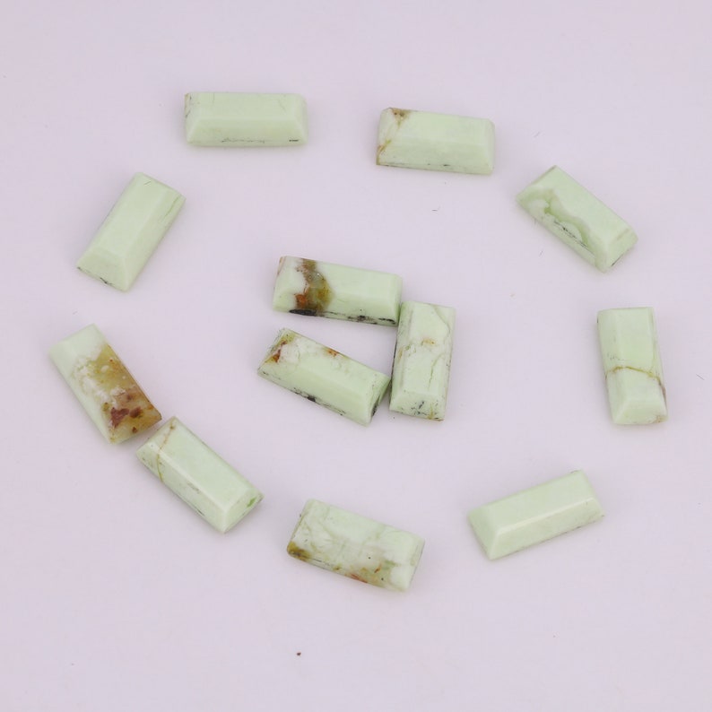 May include: A collection of twelve green, rectangular, polished, gemstone cabochons. The cabochons have a light green color with brown and black inclusions.