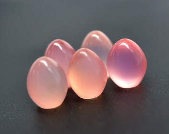 Puede incluir: Cinco piedras lisas y redondas, de color rosa y morado, que se asemejan a huevos, están dispuestas en un grupo sobre una superficie gris oscuro.