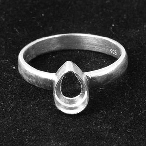 May include: A silver ring featuring a pear-shaped setting designed for a gemstone. The band has a smooth, metallic finish and the interior of the ring is clearly stamped with the number 925, indicating the sterling silver composition of the piece.