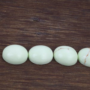 以下が含まれることがあります： 滑らかで磨かれた表面を持つ、丸い薄い緑色のカボションカットの宝石が4つ。石には、薄い茶色の筋が自然に模様のように入っている。