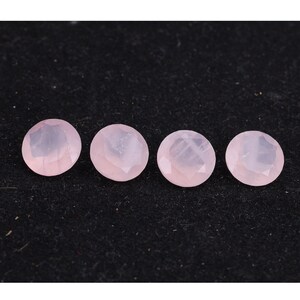 Puede incluir: Cuatro gemas redondas facetadas de cuarzo rosa dispuestas en fila sobre un fondo oscuro. Las gemas son de color rosa p&aacute;lido y tienen una superficie pulida y reflectante. Las gemas probablemente se utilizan para la fabricaci&oacute;n de joyas.