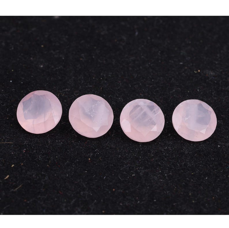 Puede incluir: Cuatro gemas redondas facetadas de cuarzo rosa dispuestas en fila sobre un fondo oscuro. Las gemas son de color rosa p&aacute;lido y tienen una superficie pulida y reflectante. Las gemas probablemente se utilizan para la fabricaci&oacute;n de joyas.