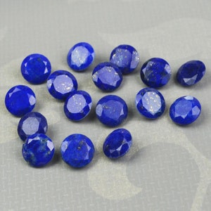 Puede incluir: Una colección de 15 piedras preciosas de lapislázuli de forma ovalada. Las piedras son de color azul intenso con motas de pirita dorada.