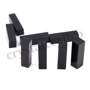 Puede incluir: Ocho piezas de obsidiana pulida de forma rectangular prismática, de color negro. Las piezas están dispuestas en un patrón escalonado sobre una superficie blanca.