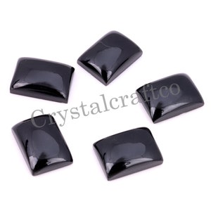 Può includere: Cinque cabochon rettangolari neri, ognuno con una superficie liscia e lucida. I cabochon sono disposti a semicerchio su uno sfondo bianco.