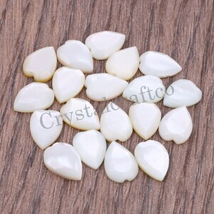 May include: A collection of white mother of pearl leaf shaped cabochons. The cabochons are smooth and have a pearlescent sheen.