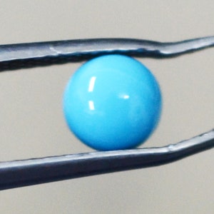 May include: A bright blue round bead held by tweezers.