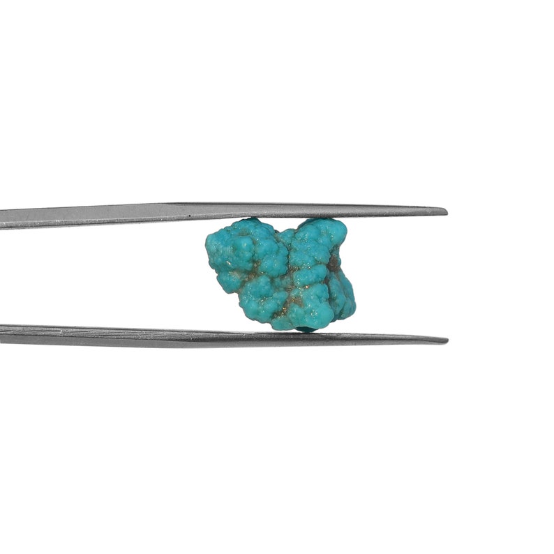 May include: A turquoise gemstone held by tweezers. The turquoise is a vibrant blue-green color and has a rough, natural texture.
