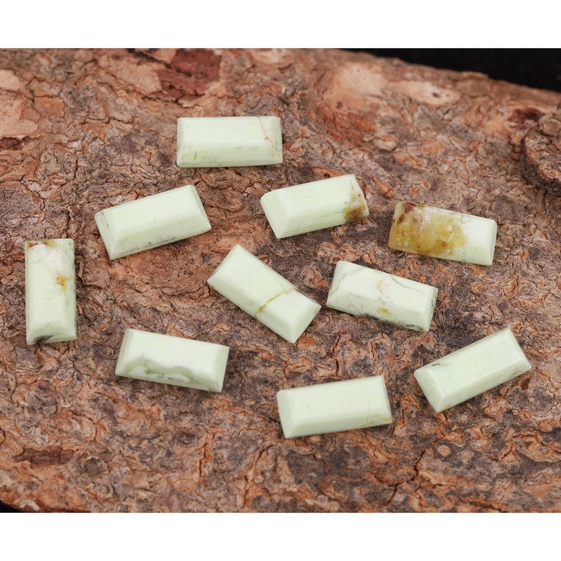 May include: Ten green and white rectangular gemstones on a brown wooden surface.