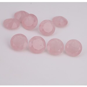 Puede incluir: Una colecci&oacute;n de gemas redondas de cuarzo rosa facetadas. Las gemas son de color rosa suave y tienen una superficie pulida y reflectante. Las piedras est&aacute;n dispuestas sobre un fondo blanco.