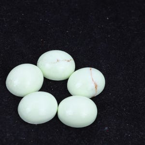 以下が含まれることがあります： 黒色の表面に、円形で滑らかで薄い緑色の、茶色の筋が入った宝石が5つ円形に並んでいます。
