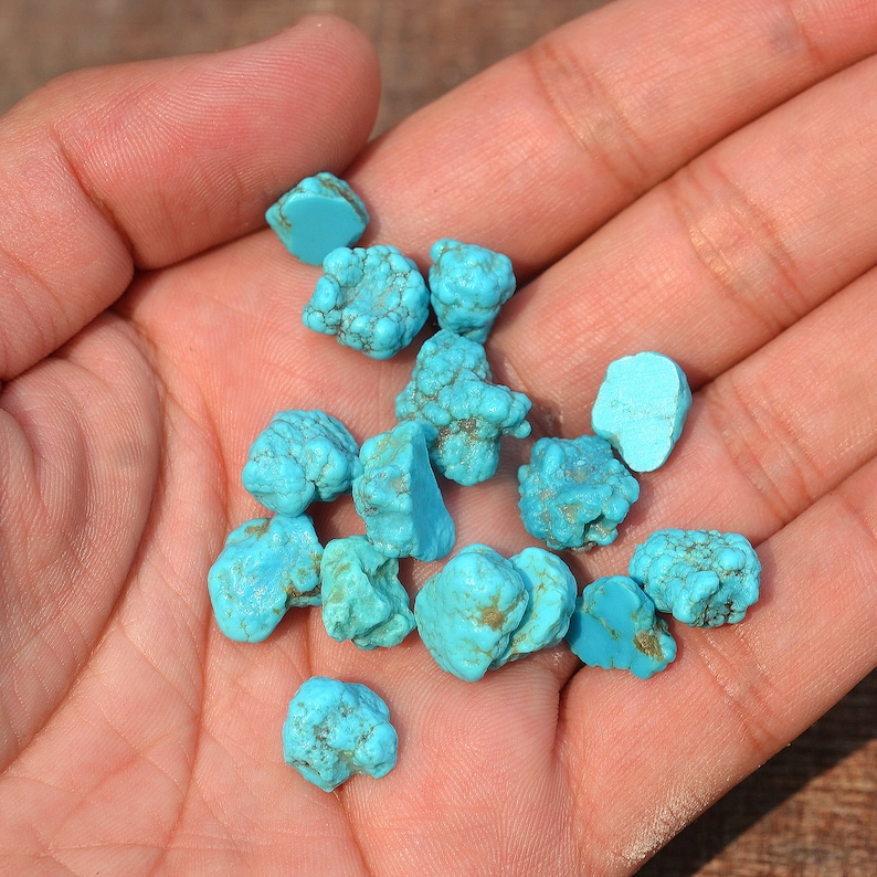 May include: A collection of turquoise stones in various shapes and sizes, ranging from light to dark blue, in a hand.