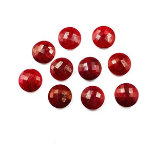 May include: Ten red gemstone cabochons, each with a faceted surface, are arranged on a white background. The cabochons are round and have a smooth, polished finish.