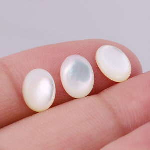 Może przedstawiać: Trzy białe, okrągłe kaboszony z perłowej masy perłowej, każdy z lekko opalizującym połyskiem.