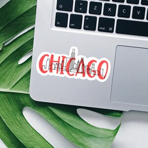 May include: A red and white sticker with a black outline of the Chicago skyline and the word "CHICAGO" in red lettering.