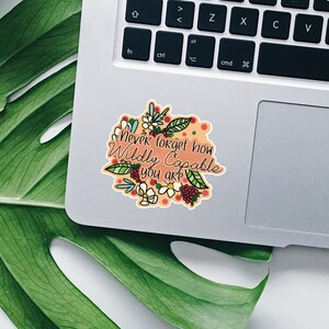 Op de afbeelding: Een sticker met een bloemenontwerp en de tekst "never forget how Wildly Capable you are" op een laptop.