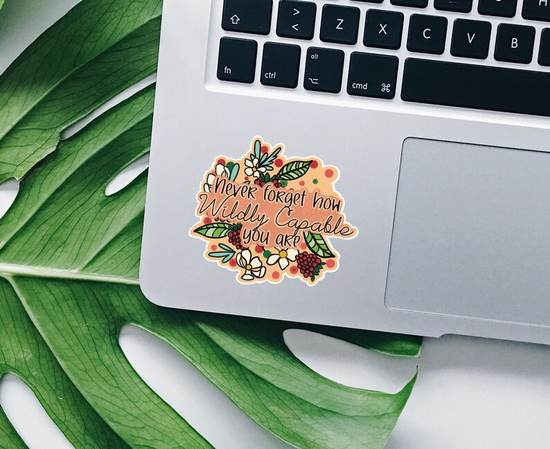 Op de afbeelding: Een sticker met een bloemenontwerp en de tekst "never forget how Wildly Capable you are" op een laptop.