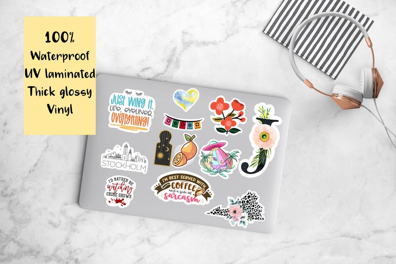 May include: A collection of waterproof, UV laminated, thick glossy vinyl stickers on a laptop. The stickers feature various designs, including floral, text-based quotes, and illustrations. A pair of headphones rests nearby.