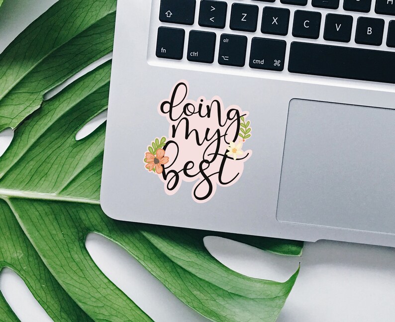 May include: A pink sticker with the text "doing my best" in black cursive lettering. The sticker is decorated with small orange and yellow flowers and green leaves.
