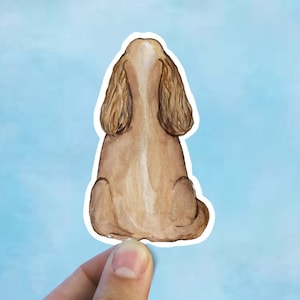 May include: Watercolor illustration of a brown and white cocker spaniel sitting with its back to the viewer.