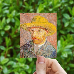 May include: A small rectangular print of Vincent van Gogh's self-portrait. The artwork features a man with a yellow straw hat, a red beard, and a blue jacket. The background is a mix of orange and brown tones, with green foliage in the background.