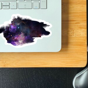 May include: A sticker featuring a watercolor-style galaxy with purple, blue, and pink hues. The galaxy is surrounded by a white border.