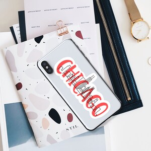 May include: A white phone case with a red and black sticker that says "Chicago" with a skyline graphic. The sticker is on a white phone case.