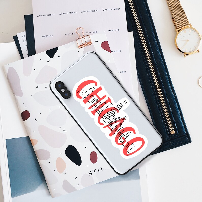 May include: A white phone case with a red and black sticker that says "Chicago" with a skyline graphic. The sticker is on a white phone case.