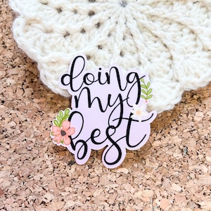 May include: A sticker with a light purple background and black text that reads "doing my best". The sticker has a floral design with pink and green flowers.