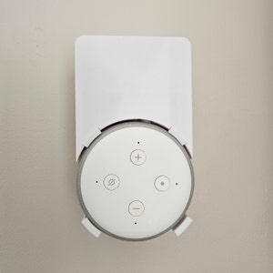 May include: White wall mount for a round, white smart speaker with four buttons. The buttons are labelled with a plus sign, a minus sign, a circle with a line through it, and a circle.
