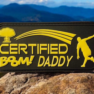 Könnte beinhalten: Ein schwarzer Patch mit gelbem Text und einer Silhouette einer springenden Person. Der Text lautet "CERTIFIED B&M! DADDY".