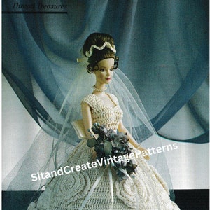 May include: A crocheted wedding dress for a doll, featuring a white lace bodice and a full skirt with ruffles. The doll is wearing a white veil and holding a bouquet of blue flowers.
