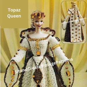 以下が含まれることがあります： 白いガウンに茶色のトリムと金の装飾が施された、女王の衣装を着たかぎ針編みの人形。人形は金の王冠をかぶり、琥珀色の宝石で飾られています。「Topaz Queen」の文字が見えます。
