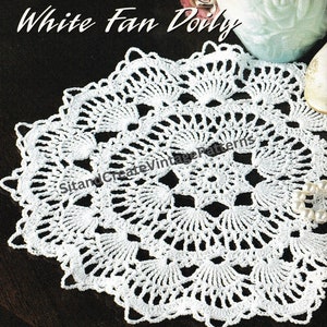 May include: White crochet doily with a fan design. The doily is made with white thread and has a delicate, lacy appearance.