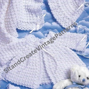 May include: A crochet baby set in white with 10 projects. The set includes a jacket, a bonnet, booties, and a blanket. The set is laid out on a blue and white background with a white teddy bear.