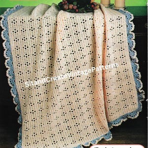 May include: A crocheted afghan in cream with a blue scalloped border. The afghan has an eyelet pattern and is draped over a surface. The text "Eyelet Delight Afghan" is at the top. The text "Illuminate your decor with this striking peach and lilac duet" is at the bottom.