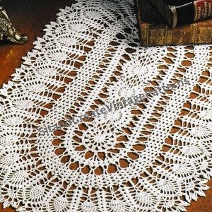 Puede incluir: Un camino de mesa ovalado de ganchillo blanco con un delicado patrón floral. El camino de mesa está hecho con un hilo fino y tiene un aspecto de encaje.